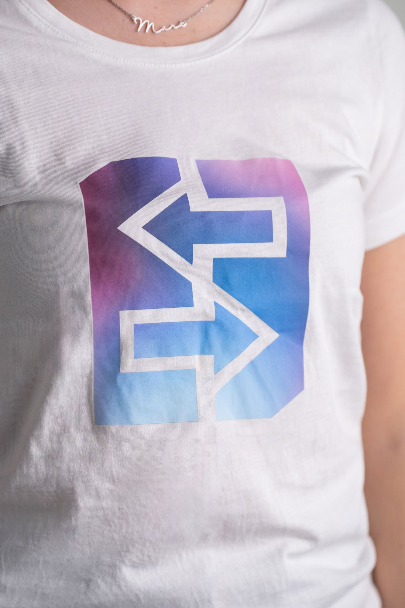Eine Frau trägt ein weißes T-Shirt mit einem blauen und pinken Logo, ideal für den Miami-Lifestyle und strahlende Sonnenuntergänge.