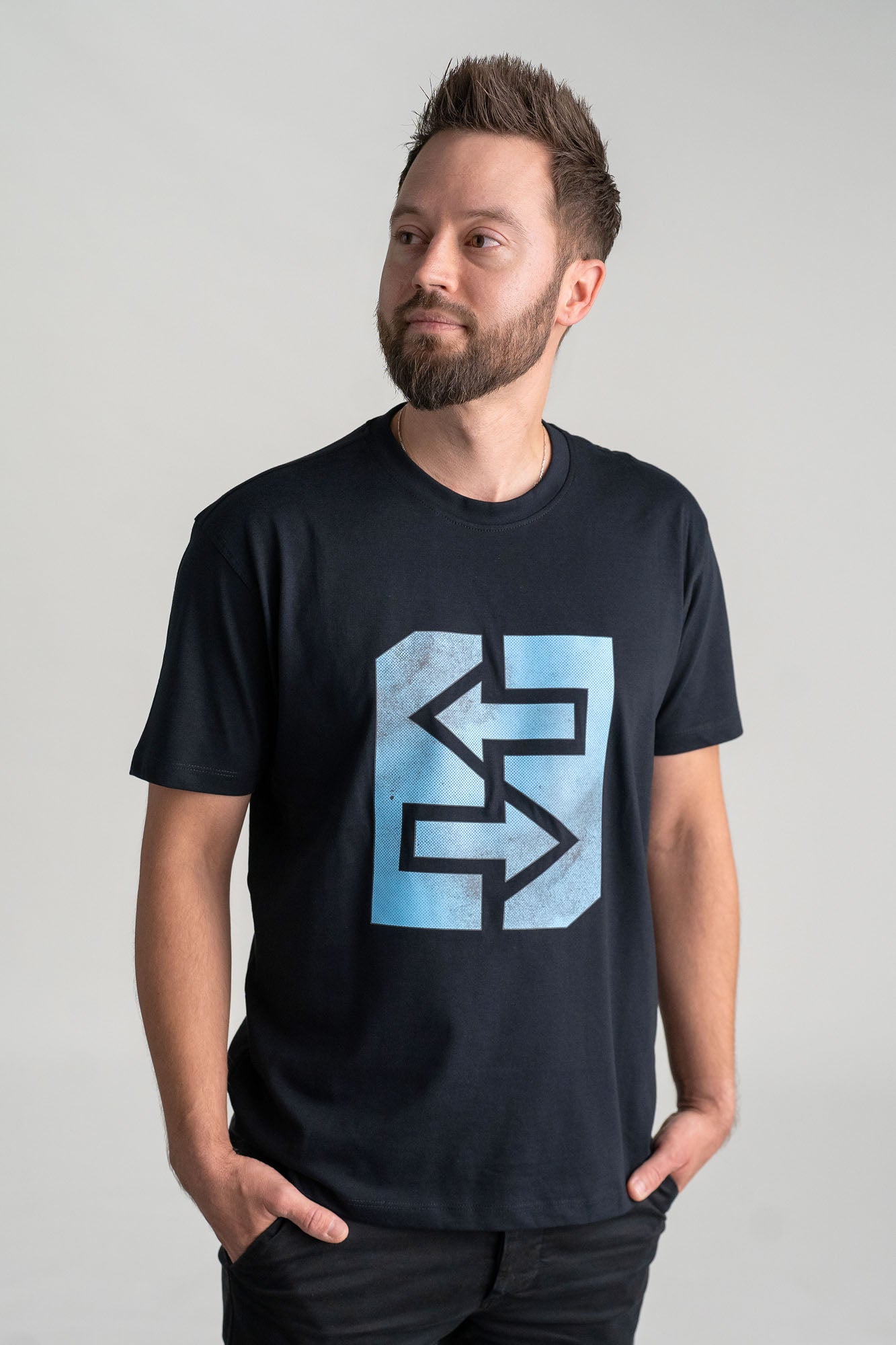 Ein Mann trägt ein schwarzes T-Shirt mit einem blauen Logo, inspiriert von griechischer Mythologie und Geschichte.