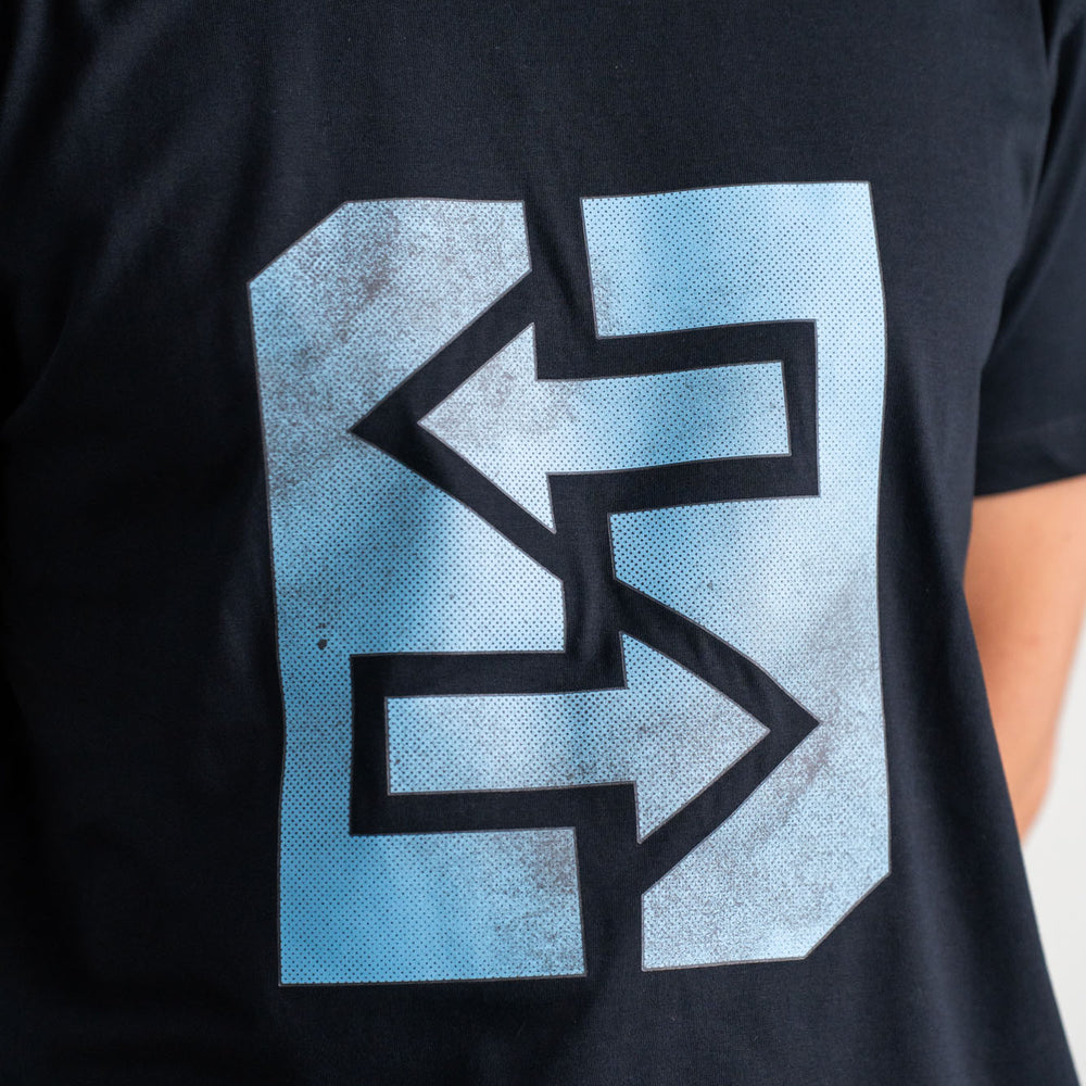 Ein Mann trägt ein schwarzes T-Shirt mit einem blauen Logo, inspiriert von griechischer Mythologie und Geschichte.