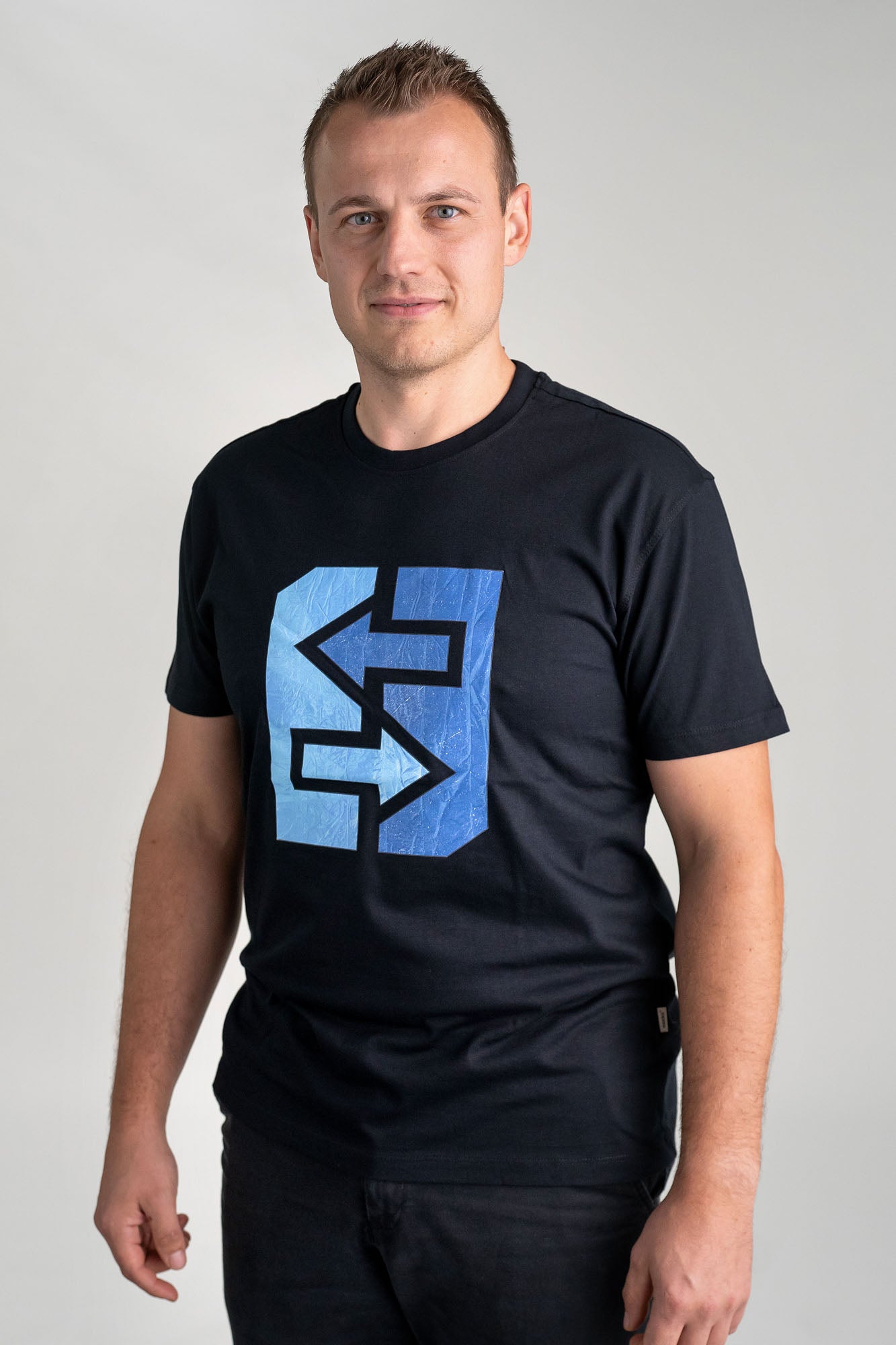 Ein Mann trägt ein schwarzes T-Shirt mit einem blauen Logo, das frischen Wind und nordische Coolness symbolisiert.