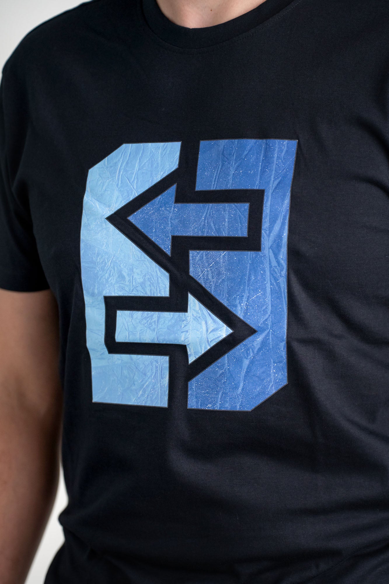Ein Mann trägt ein schwarzes T-Shirt mit einem blauen Logo, das frischen Wind und nordische Coolness symbolisiert.