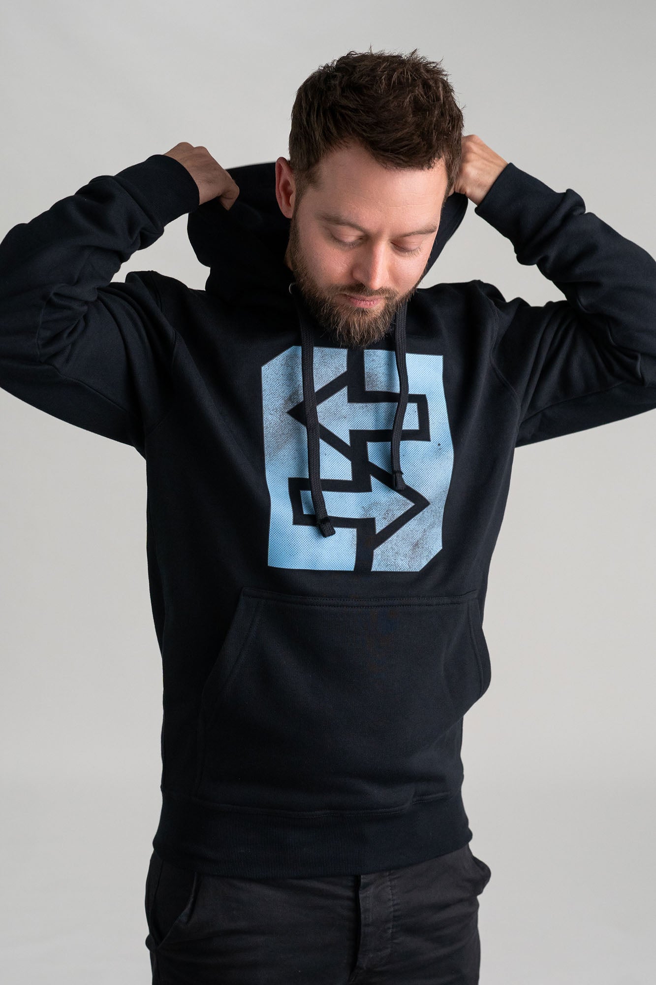 Ein Mann trägt einen schwarzen Kapuzenpullover mit einem blauen Logo darauf.