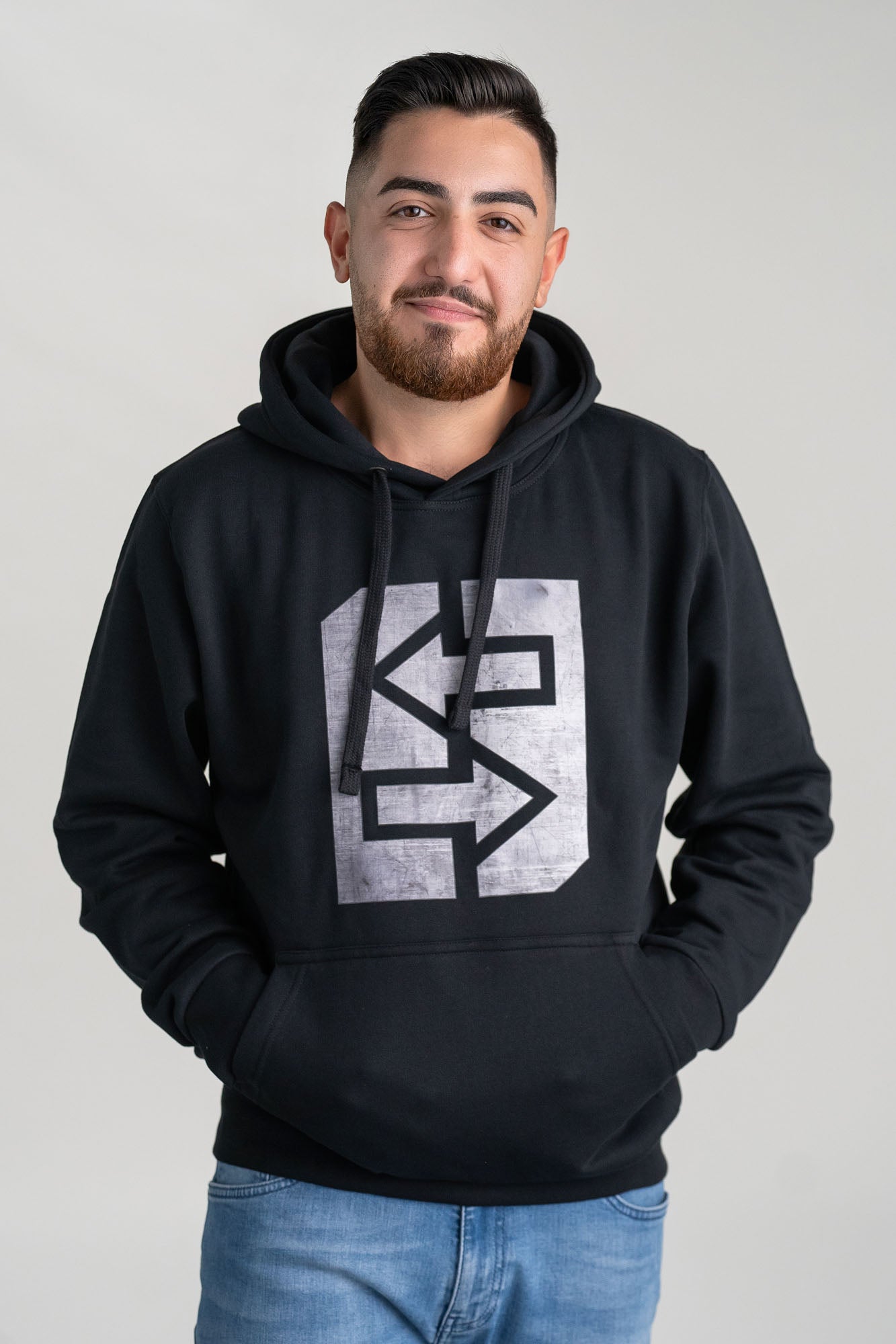 Ein Mann trägt einen schwarzen Hoodie mit einem grauen Grafikdesign.