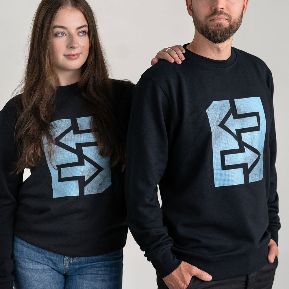 Ein Mann und eine Frau tragen schwarze Sweatshirts mit einem Logo, inspiriert von griechischer Mythologie und Geschichte.