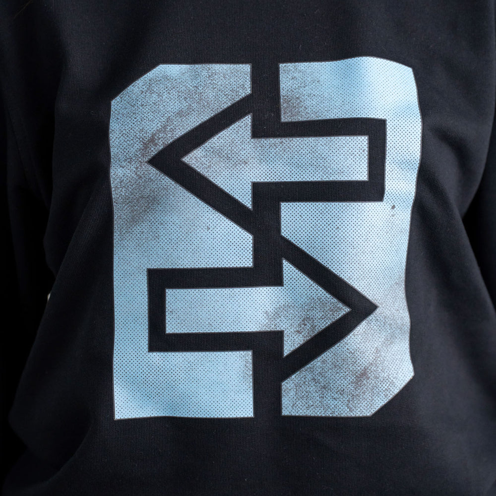 
                      
                        Eine Frau trägt ein schwarzes Sweatshirt mit einem blauen Logo, inspiriert von griechischer Mythologie und Geschichte.

                      
                    