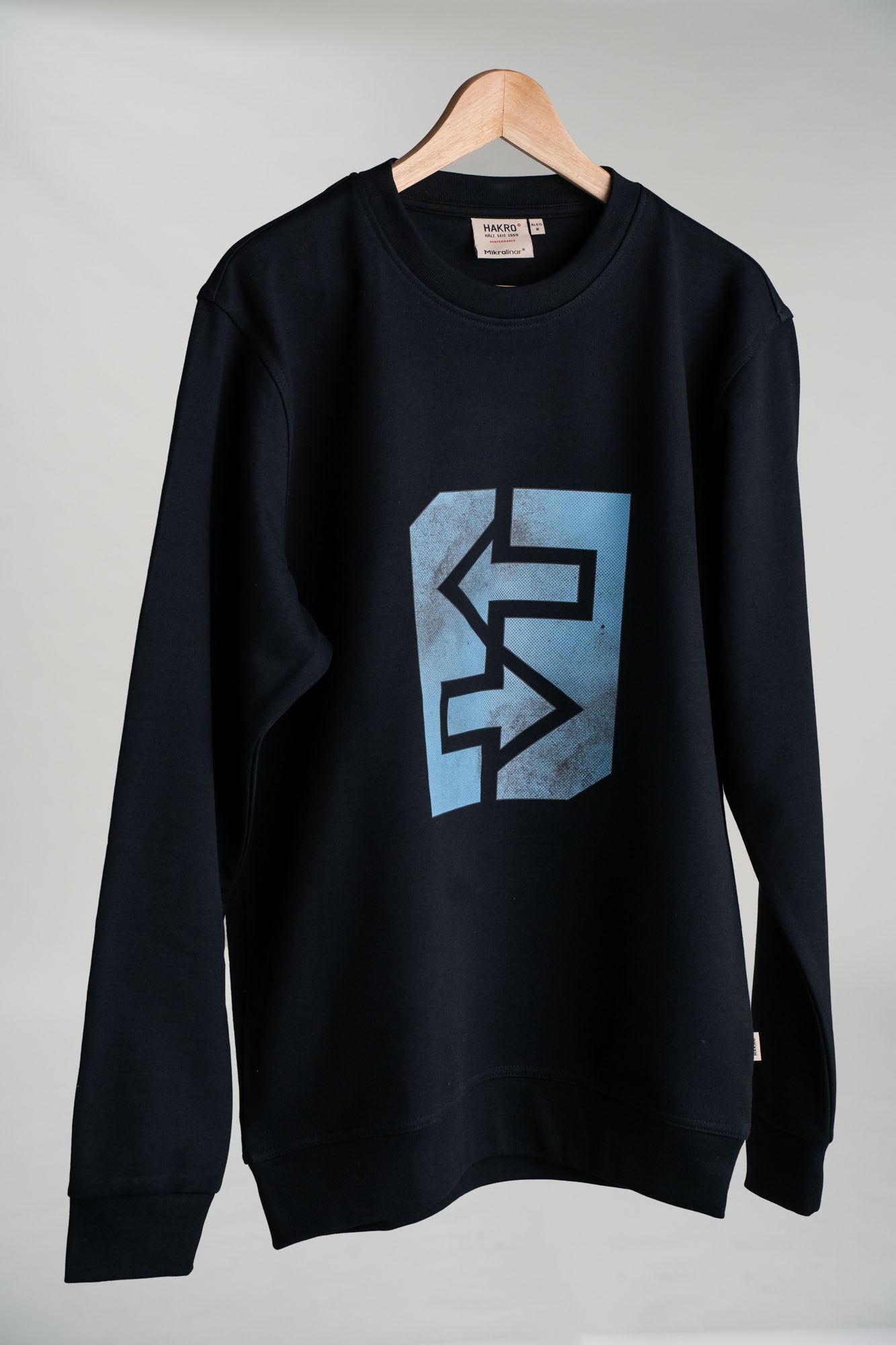 Schwarzes Sweatshirt mit blauem Logo, inspiriert von griechischer Mythologie und rustikaler Architektur.