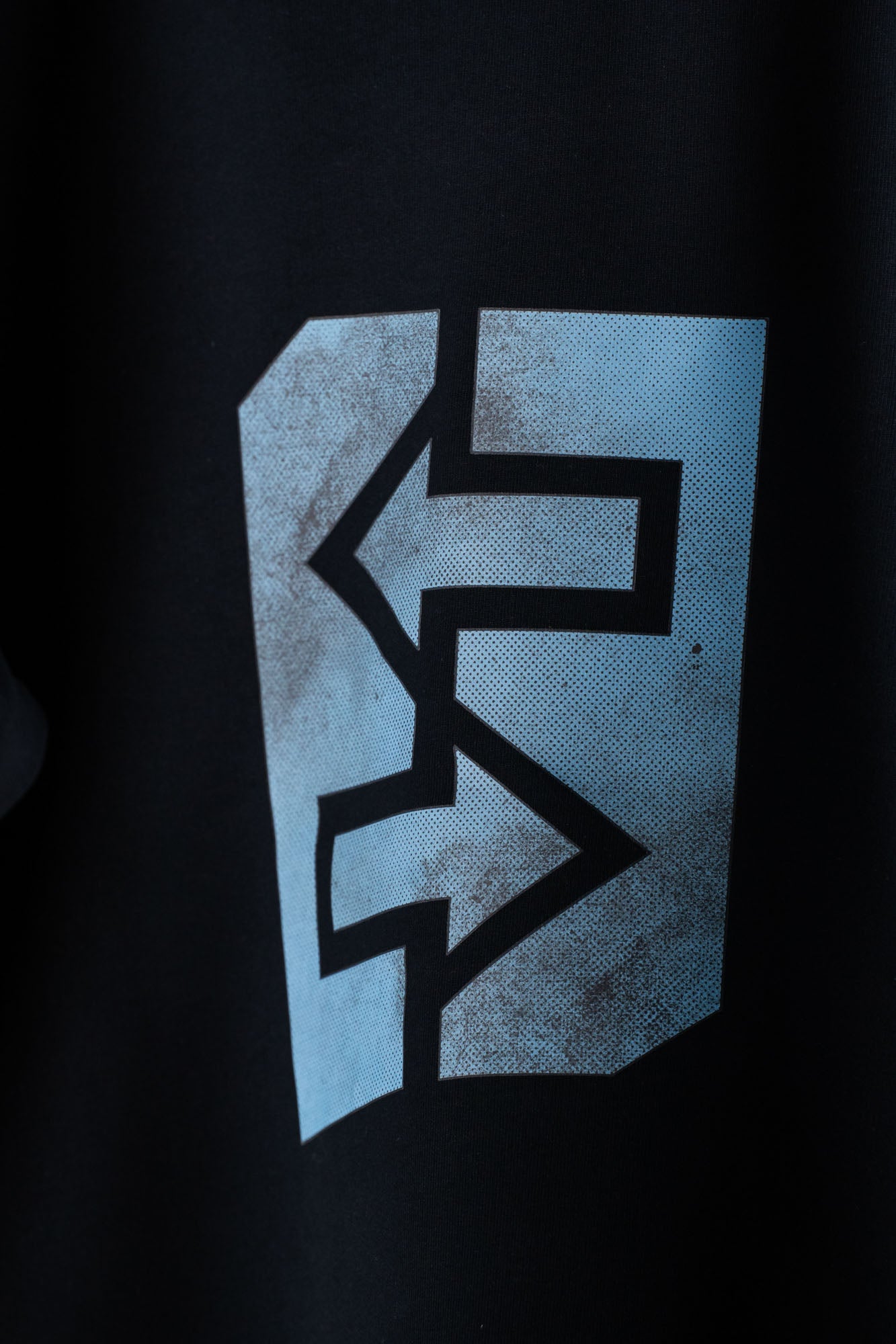 Schwarzes T-Shirt mit blauem Logo, inspiriert von griechischer Mythologie und rustikaler Architektur.