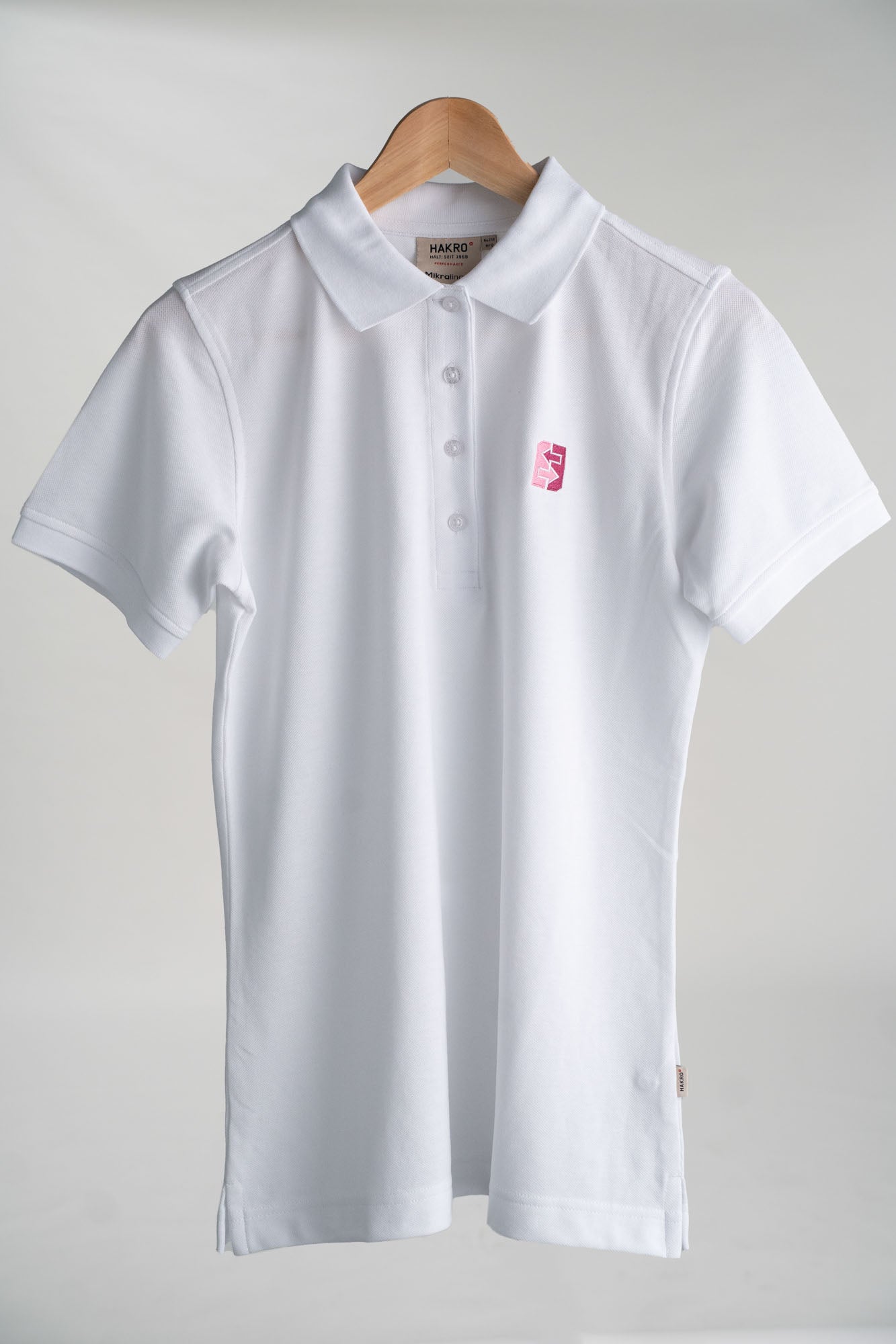 Weißes Polohemd mit pinkem Logo auf der Brust, ideal für Freizeit und Büro, vereint Stil und Funktionalität.